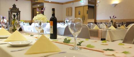 Een feestzaal met ronde tafels gedekt voor een formeel evenement, met witte tafelkleden, netjes gerangschikte borden en wijnglazen.