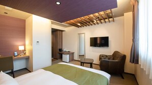 Habitación de hotel con cama, escritorio, silla, televisor y espejo.