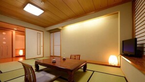 Una habitación japonesa tradicional con suelo de tatami, una mesa baja de madera y un televisor sobre un mueble de madera.