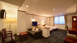 Habitación de hotel con sofá, escritorio, televisión, cama y ventana con cortinas.