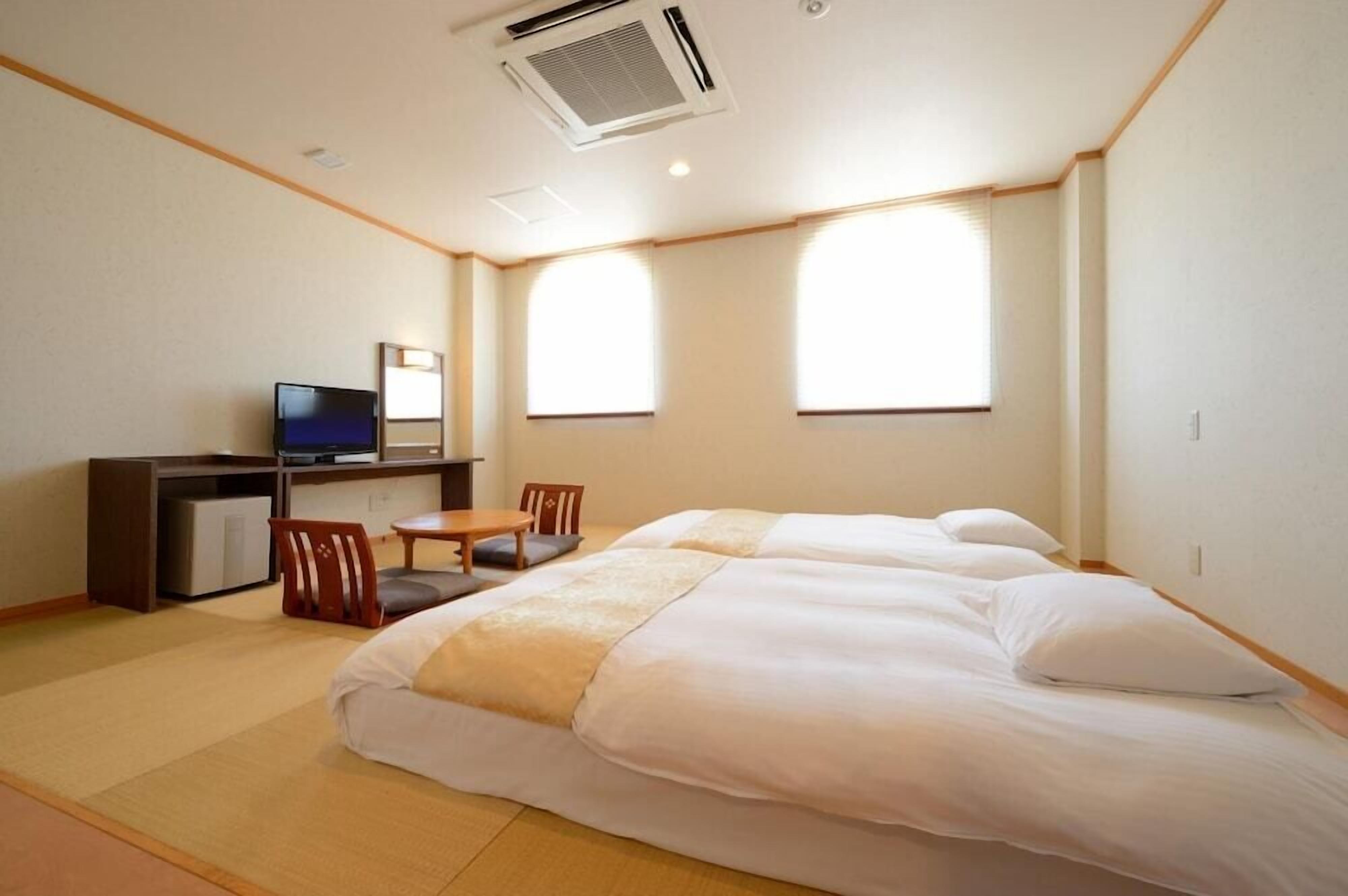 Une chambre d’hôtel avec deux lits, un bureau avec une télévision et une chaise.