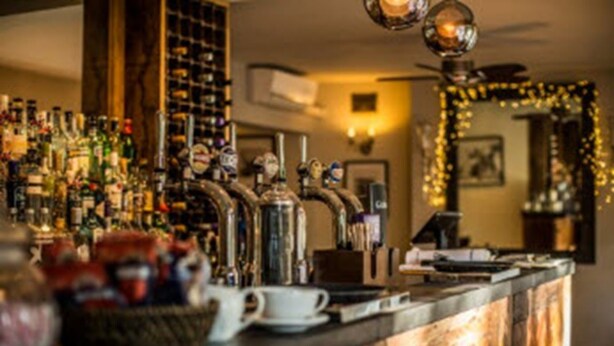 A bar area with multiple liquor bottles, a coffee machine, and a cash register. - The Peel Aldergate (Tamworth)