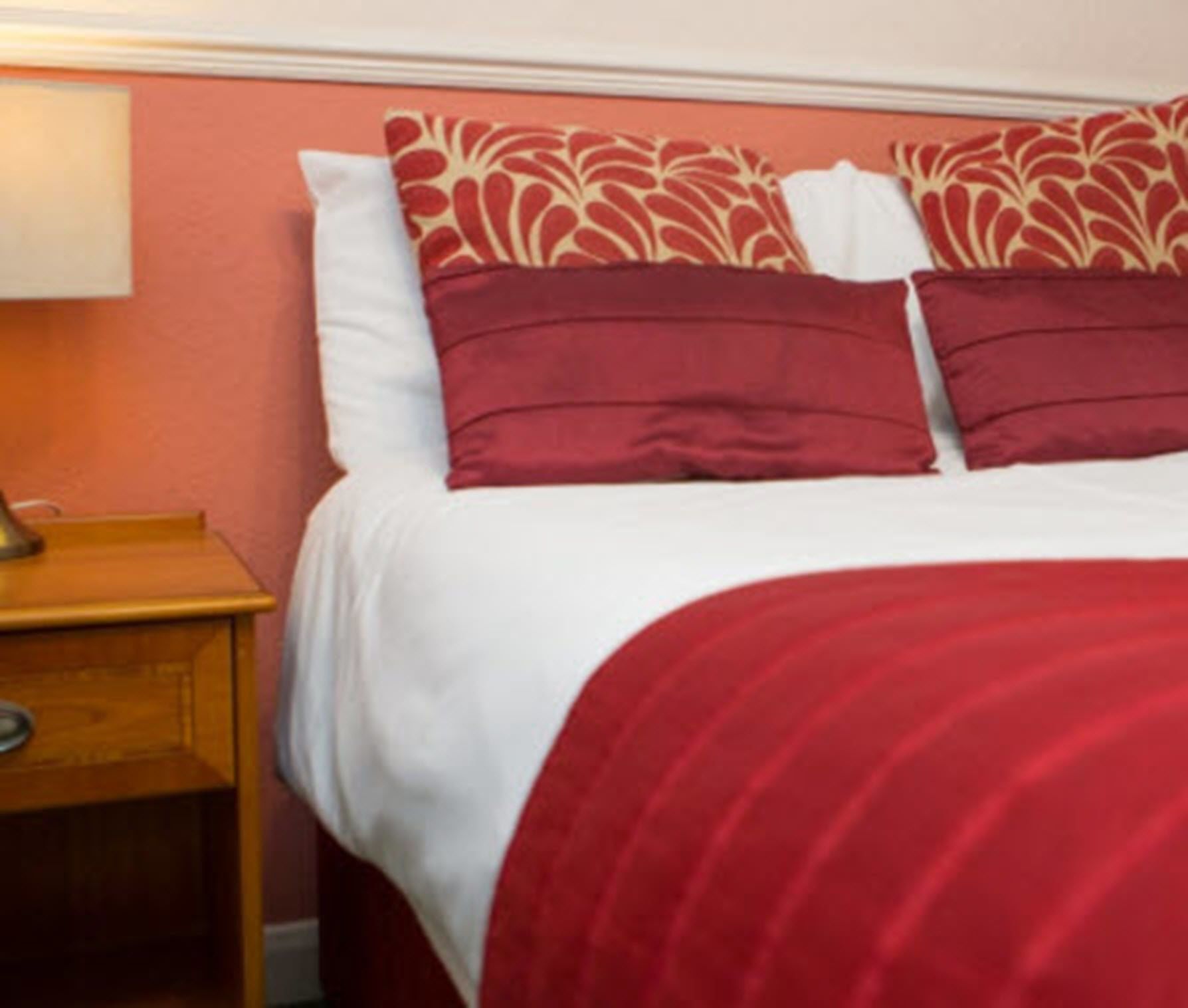 A hotel room with a bed, pillows, and a nightstand.