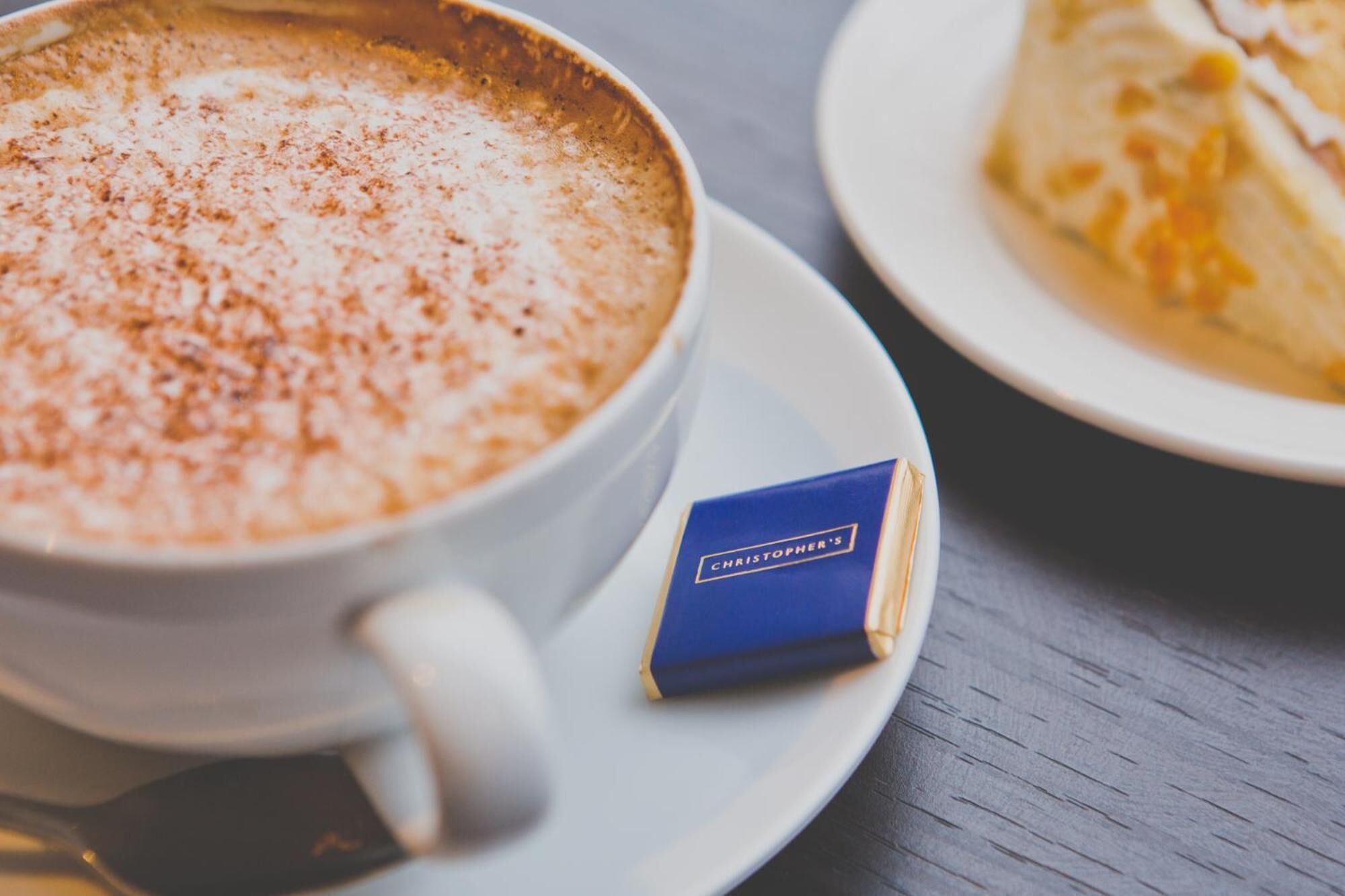 A cup of coffee with a blue packet labeled "Christopher's" on a saucer.