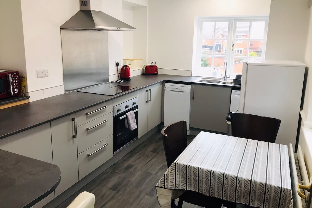 Uma cozinha moderna com fogão, forno e lava-louças, uma mesa de jantar com toalha listrada e uma janela com vista para edifícios.