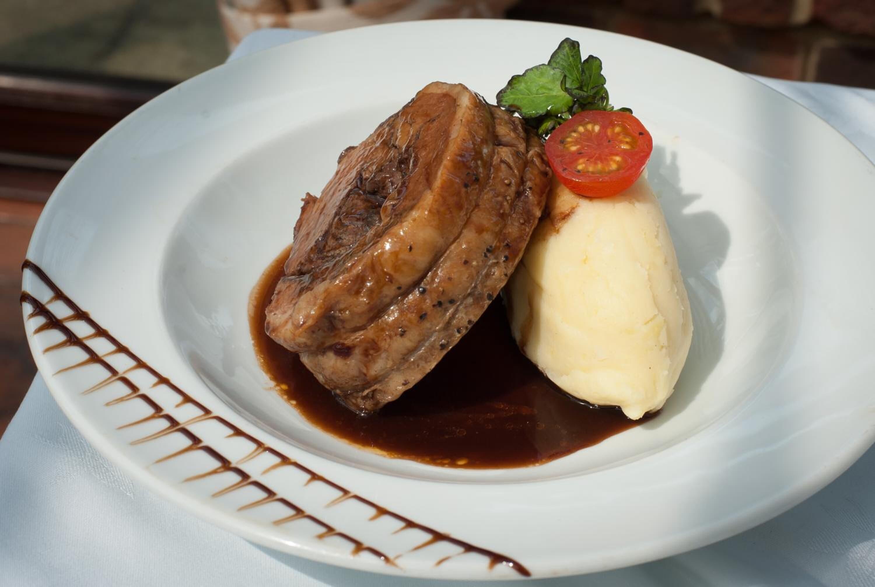 A plate with a piece of meat, mashed potatoes, and a slice of tomato.