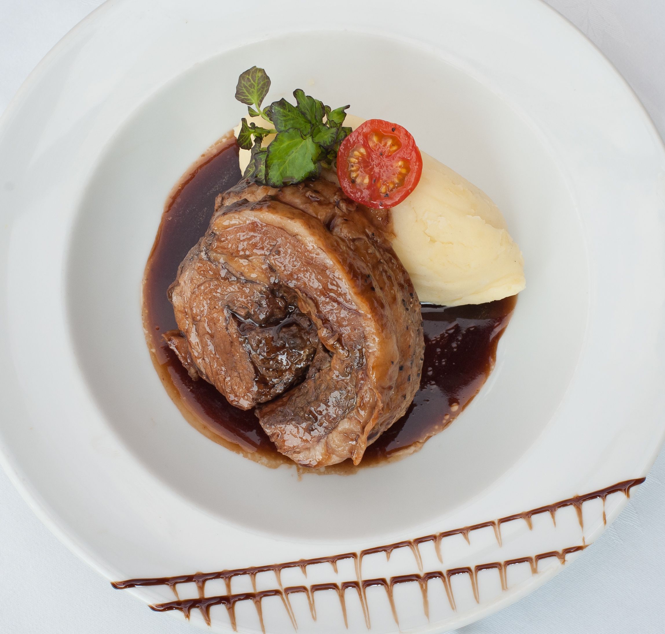 A plate with a meat dish, mashed potatoes, and a tomato slice.