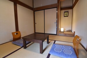 A traditional Japanese room with tatami flooring, a wooden table, two chairs, and sliding doors.