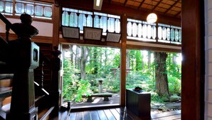 Una habitación tradicional japonesa con suelo de tatami, una escalera de madera y vistas a un área boscosa.