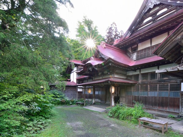 A traditional Japanese building with a red tiled roof, surrounded by lush greenery and a small garden area.