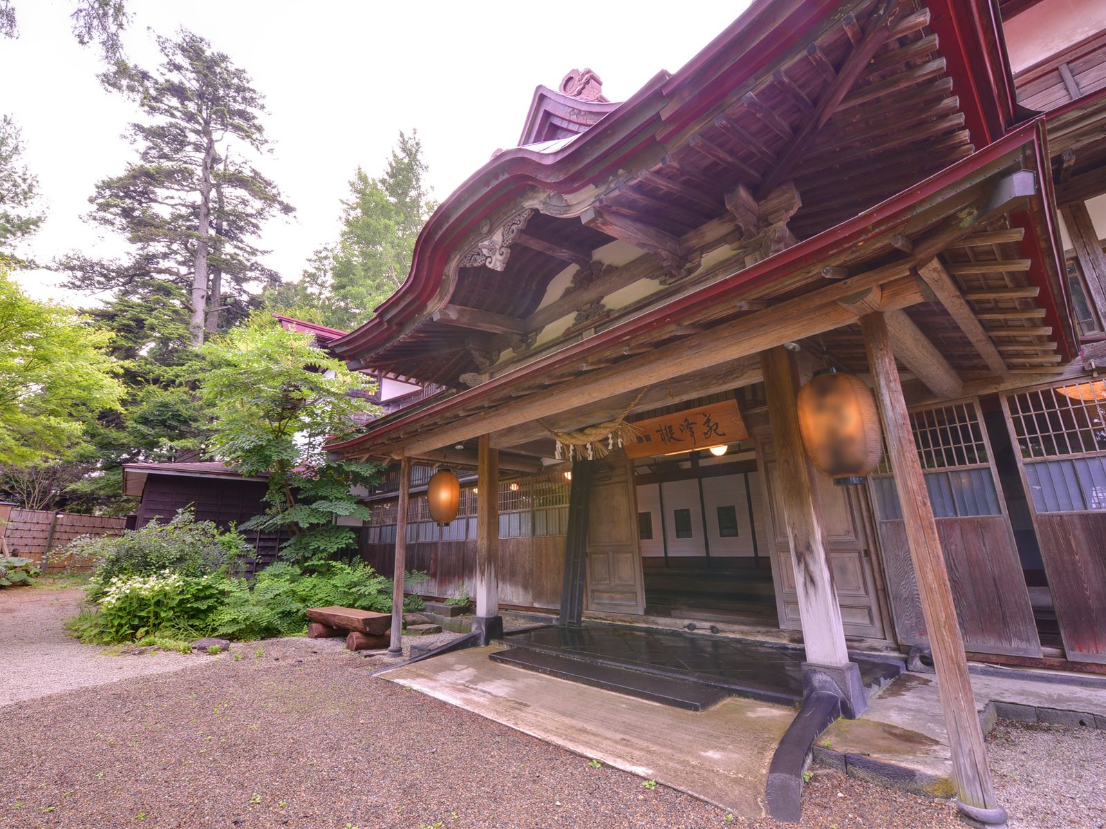 A traditional Japanese building with a wooden exterior, a covered entrance, and a gravel pathway leading to the entrance.