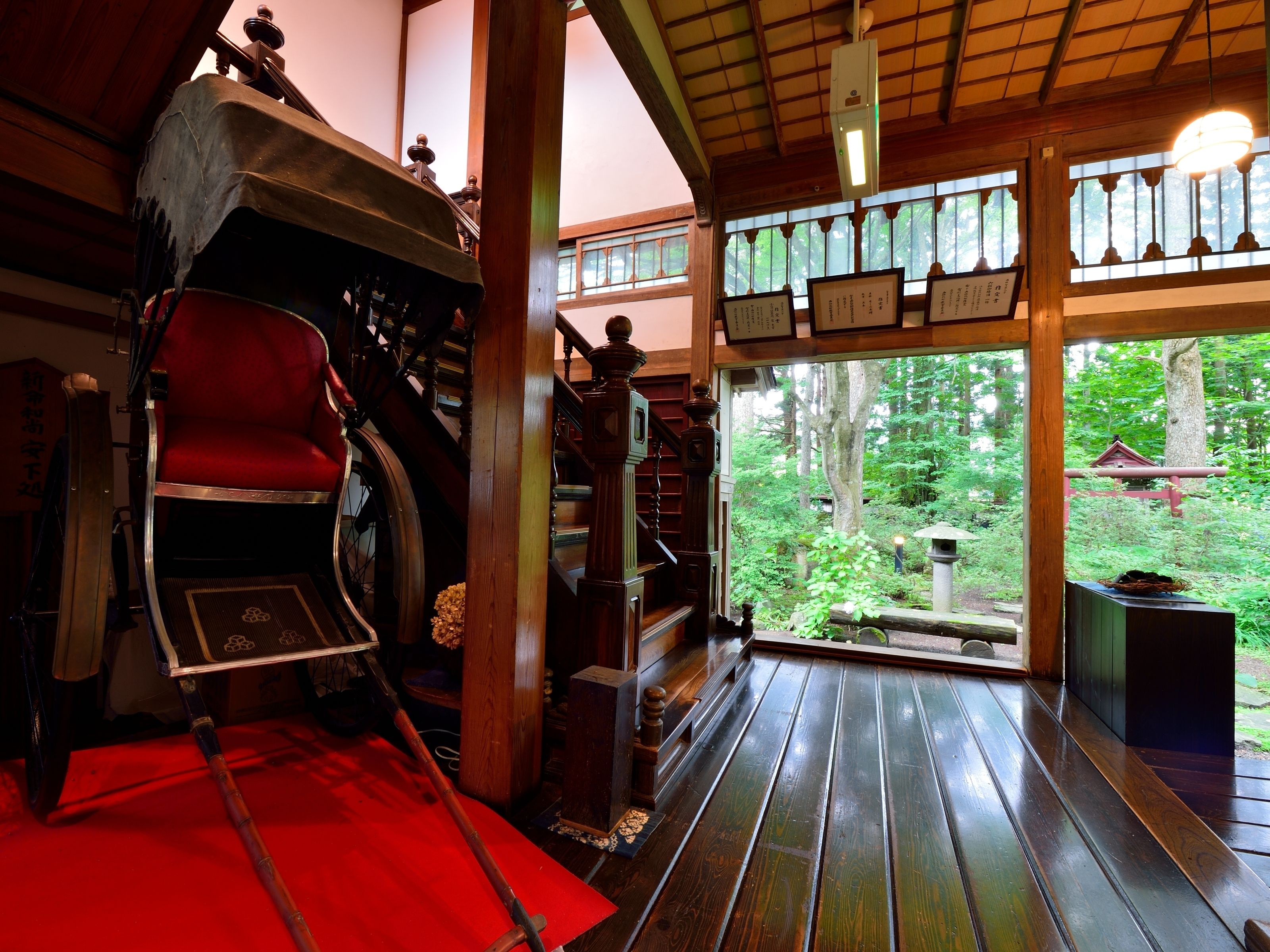 A traditional Japanese room with tatami flooring, a red futon, a sliding door leading to a forest view, and a wooden staircase.