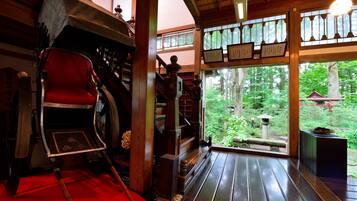 A traditional Japanese room with tatami flooring, a red futon, a sliding door leading to a forest view, and a wooden staircase.