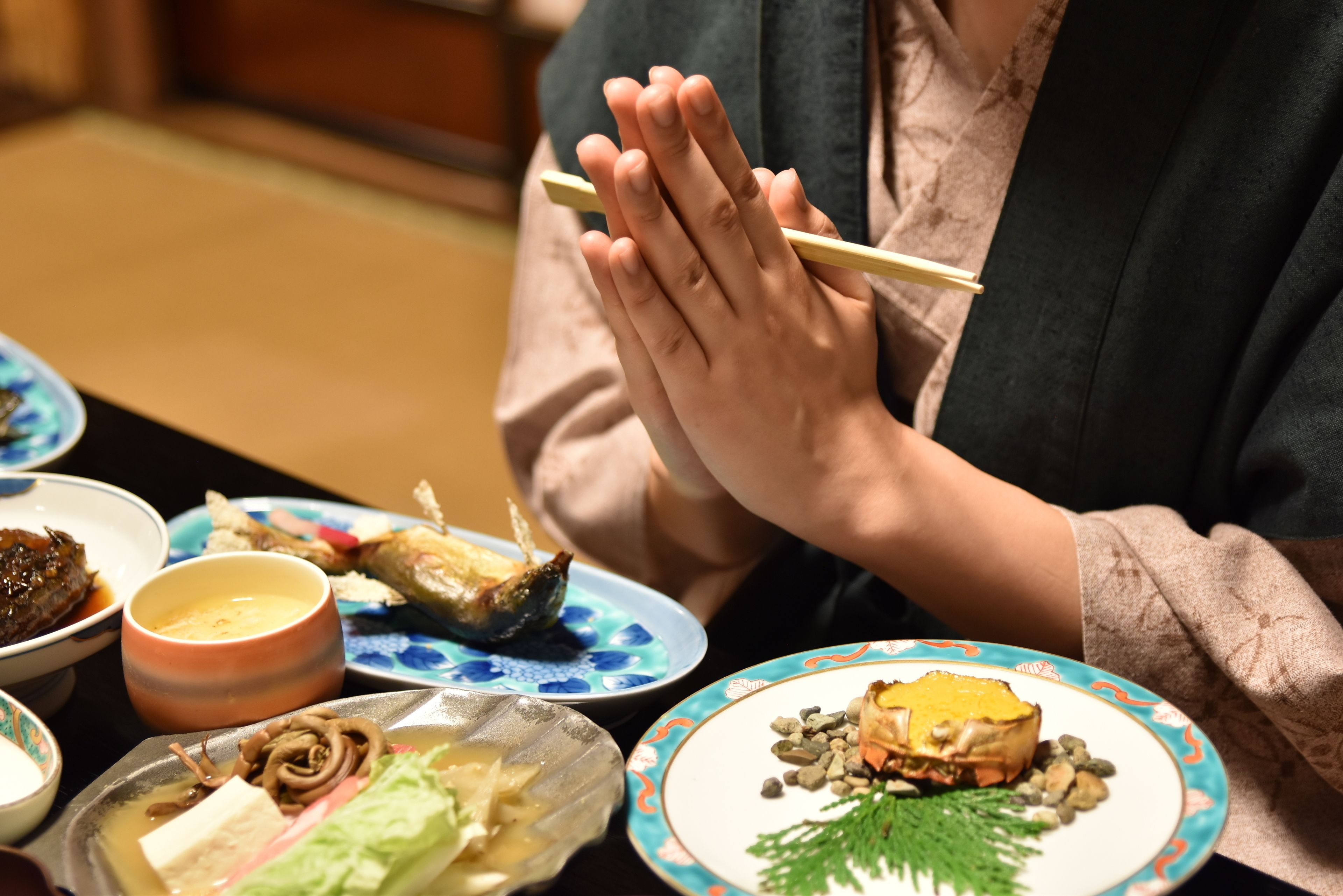 A person holding chopsticks over a plate of food, with various dishes on the table.