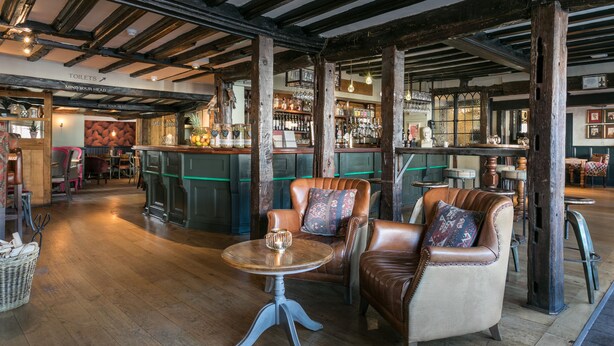 A bar area with wooden beams, leather chairs, and a round table with a candle. - White Lion Tenterden (Tenterden)