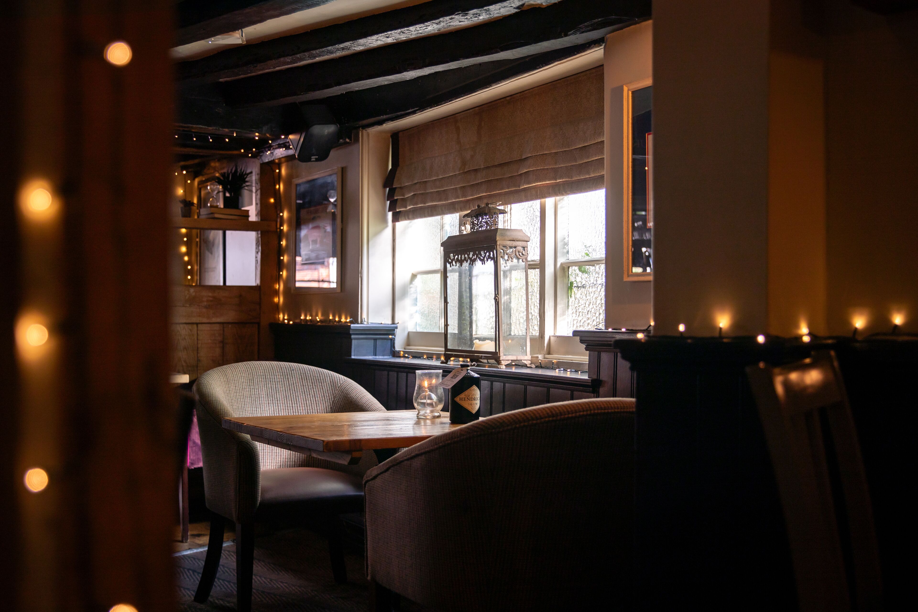 A cozy restaurant interior with wooden furniture, a window with a view, and string lights.