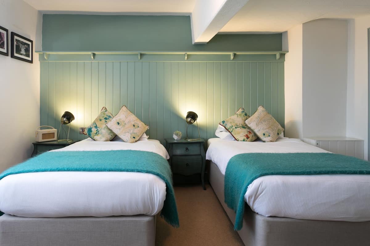 A twin bedroom with two beds, bedside tables, lamps, and a wall-mounted shelf.