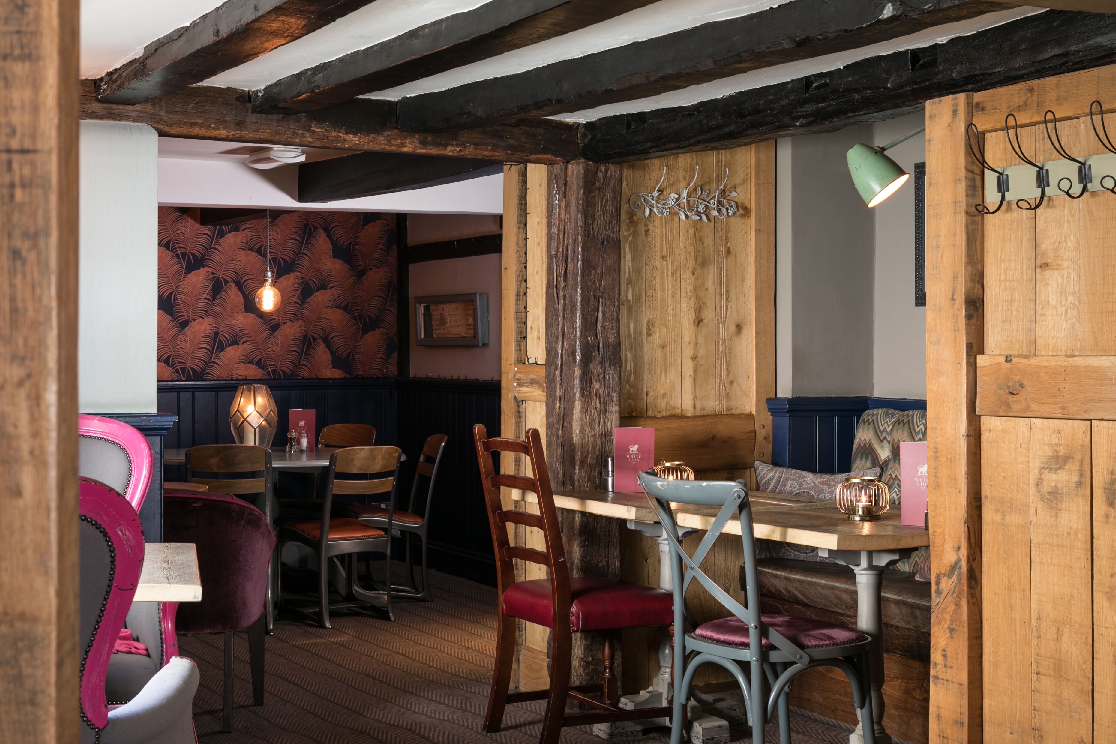 Un coin repas au style rustique, avec des poutres en bois, un mur orné de motifs et un mélange de chaises en bois et de chaises rembourrées.