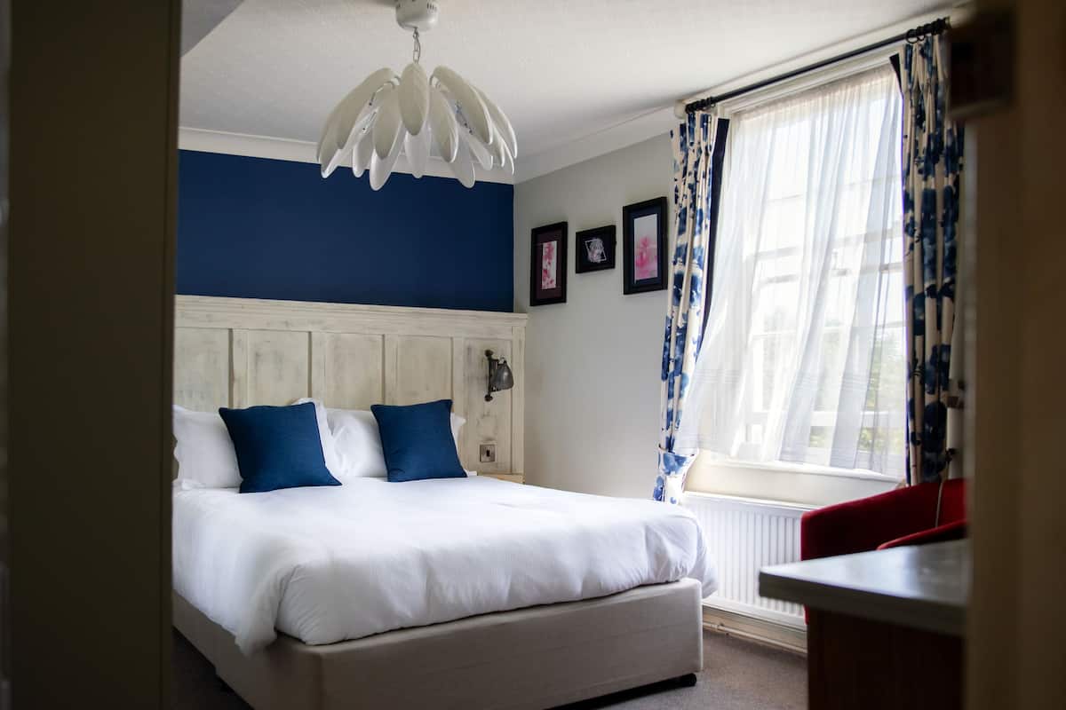 A bedroom with a bed, a window with curtains, and a wall with framed pictures.