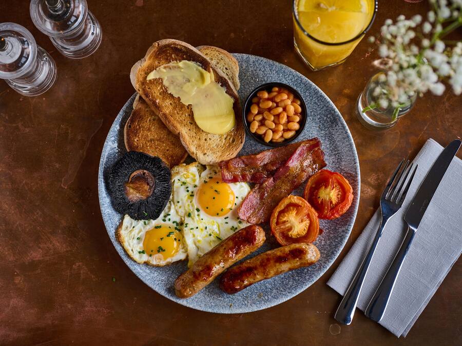A breakfast plate with toast, eggs, bacon, sausages, beans, and tomatoes.