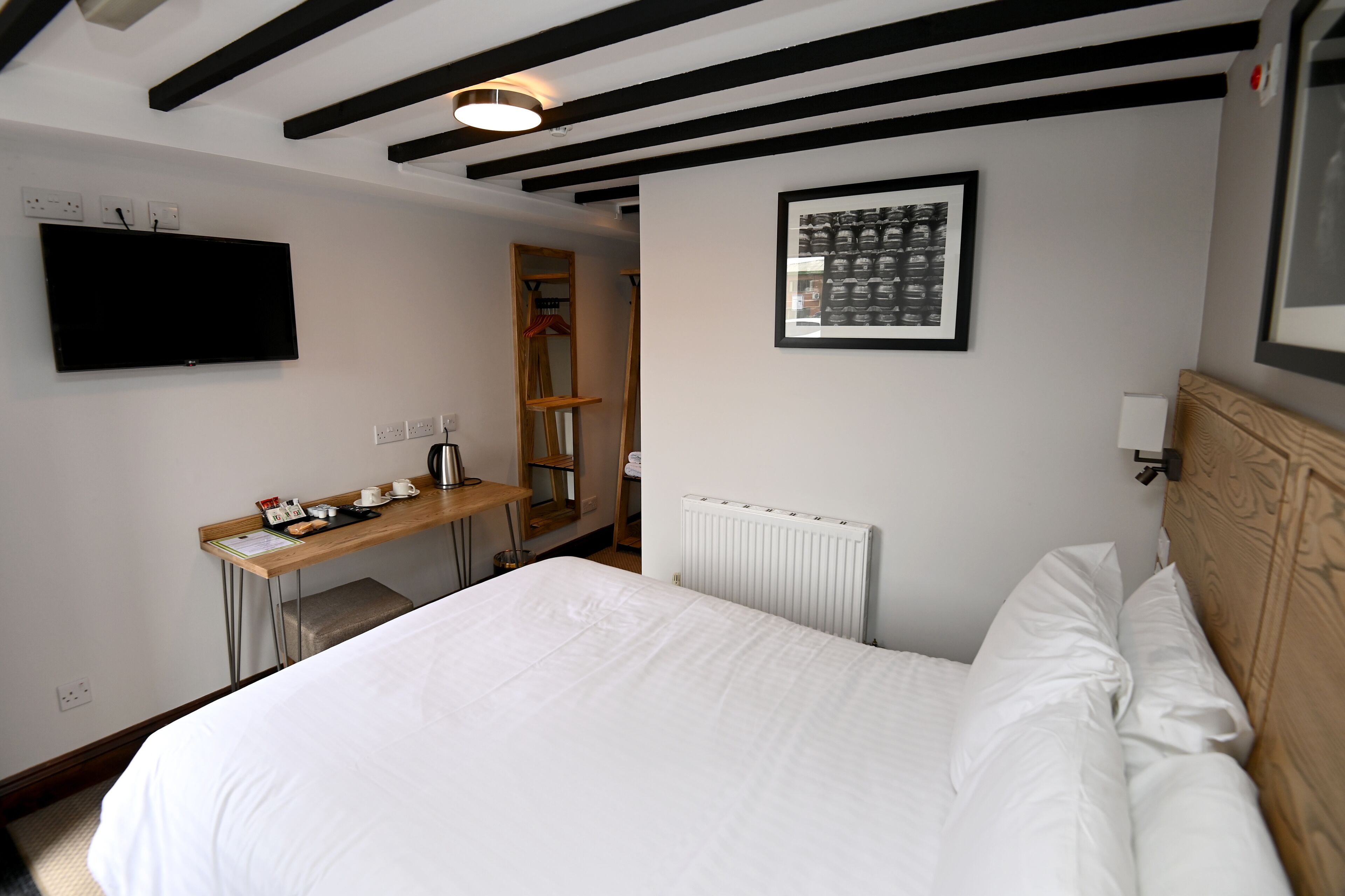 Habitación de hotel con una cama, un escritorio con teléfono y una taza, un radiador y un cuadro en la pared.