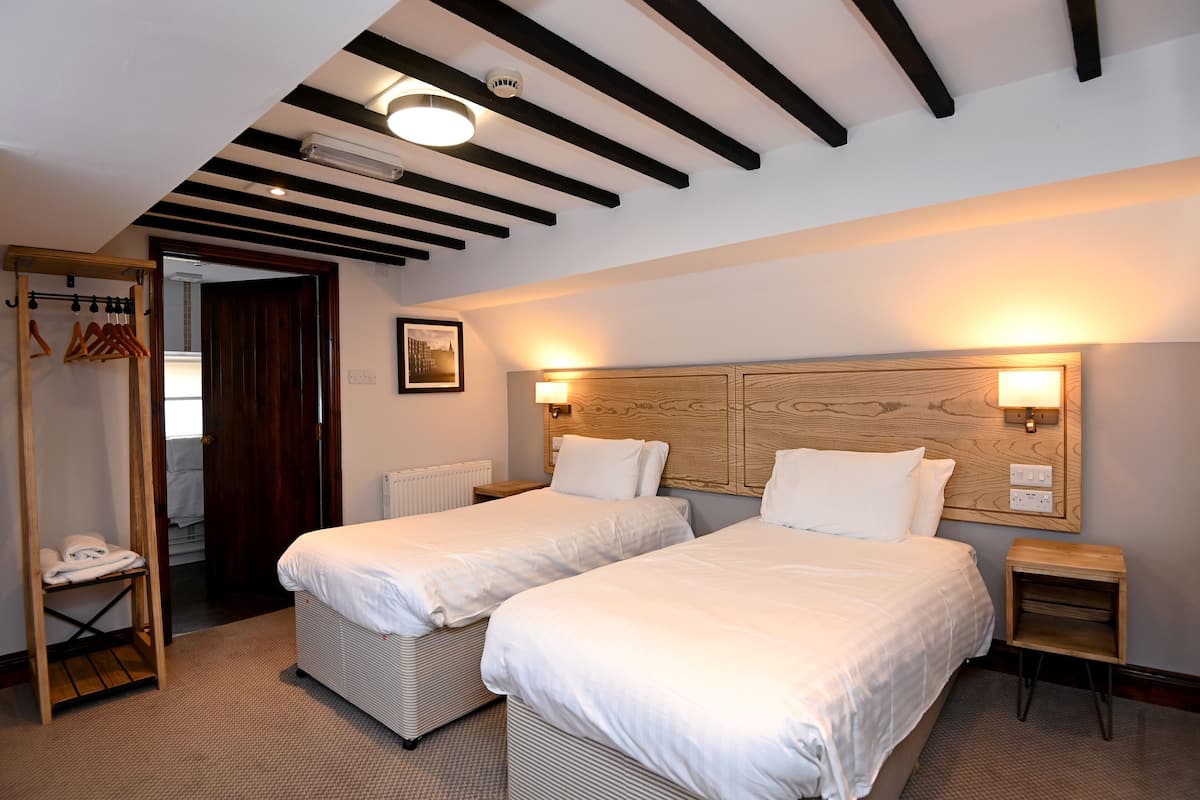 A hotel room with two beds, a wooden headboard, a small bedside table, a wardrobe, and a radiator.