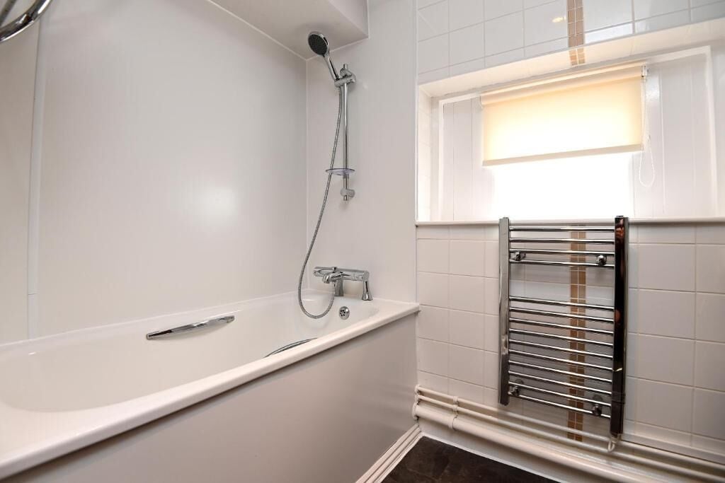 A bathroom with a white bathtub, a showerhead, and a towel rack.