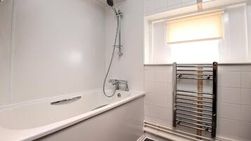 Un baño con una bañera blanca, cabezal de ducha y un perchero para toallas.