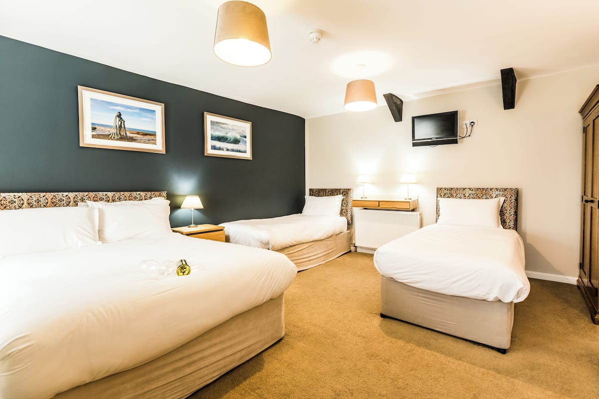 Habitación de hotel con tres camas, un televisor y obras de arte en las paredes.