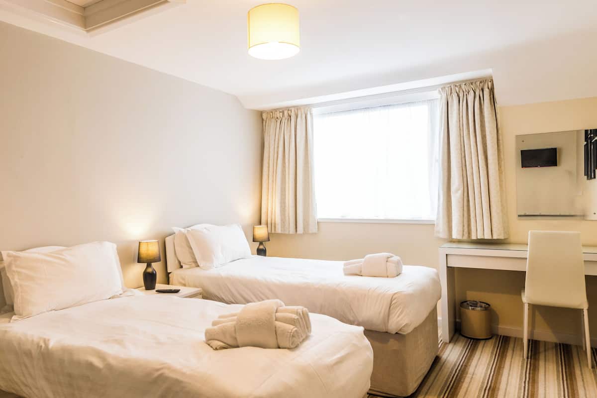 Una habitación de hotel con dos camas, un escritorio, una silla, una lámpara y un televisor.