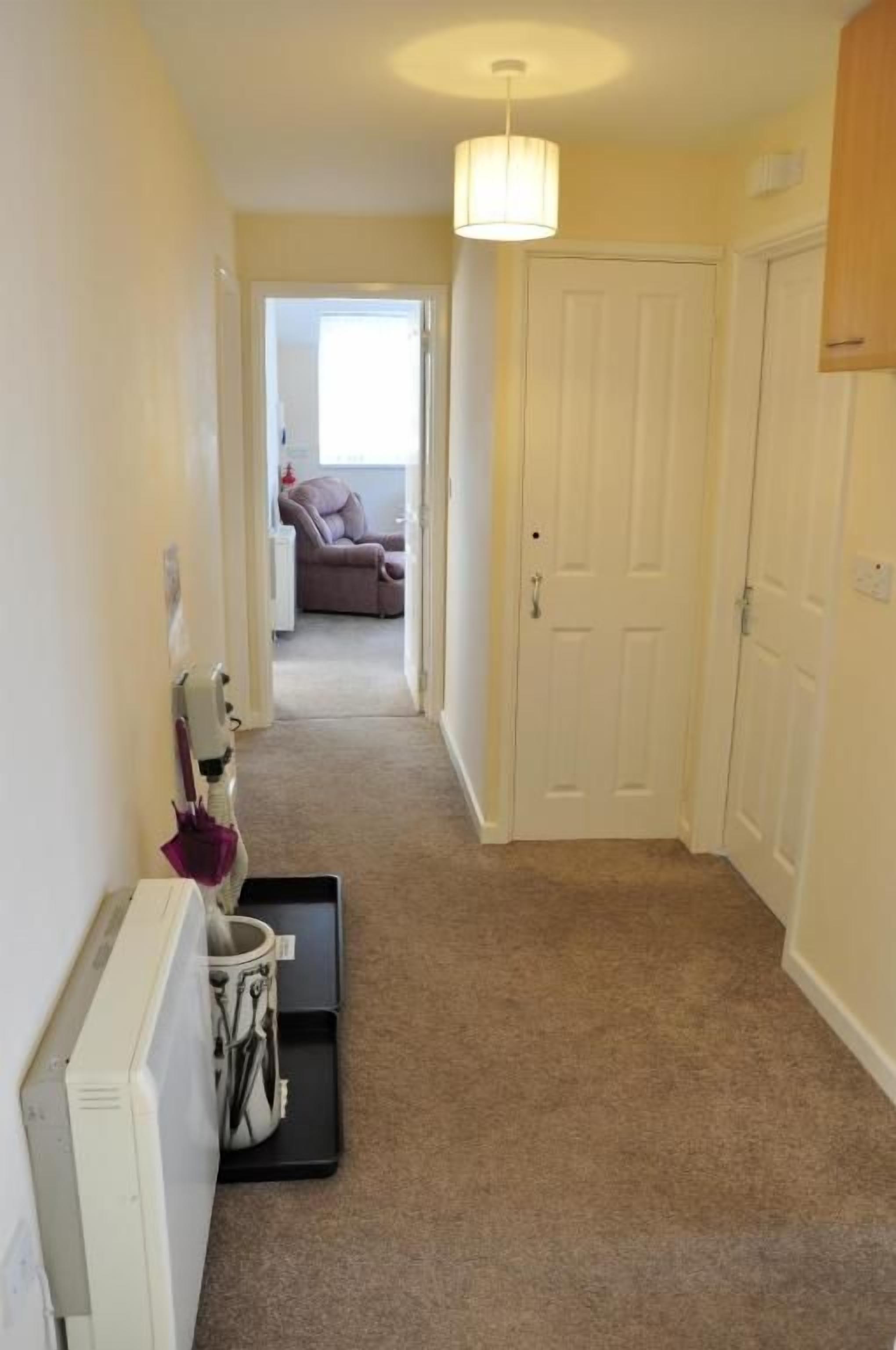 A hallway with carpeted flooring, a white door, and a radiator on the left.