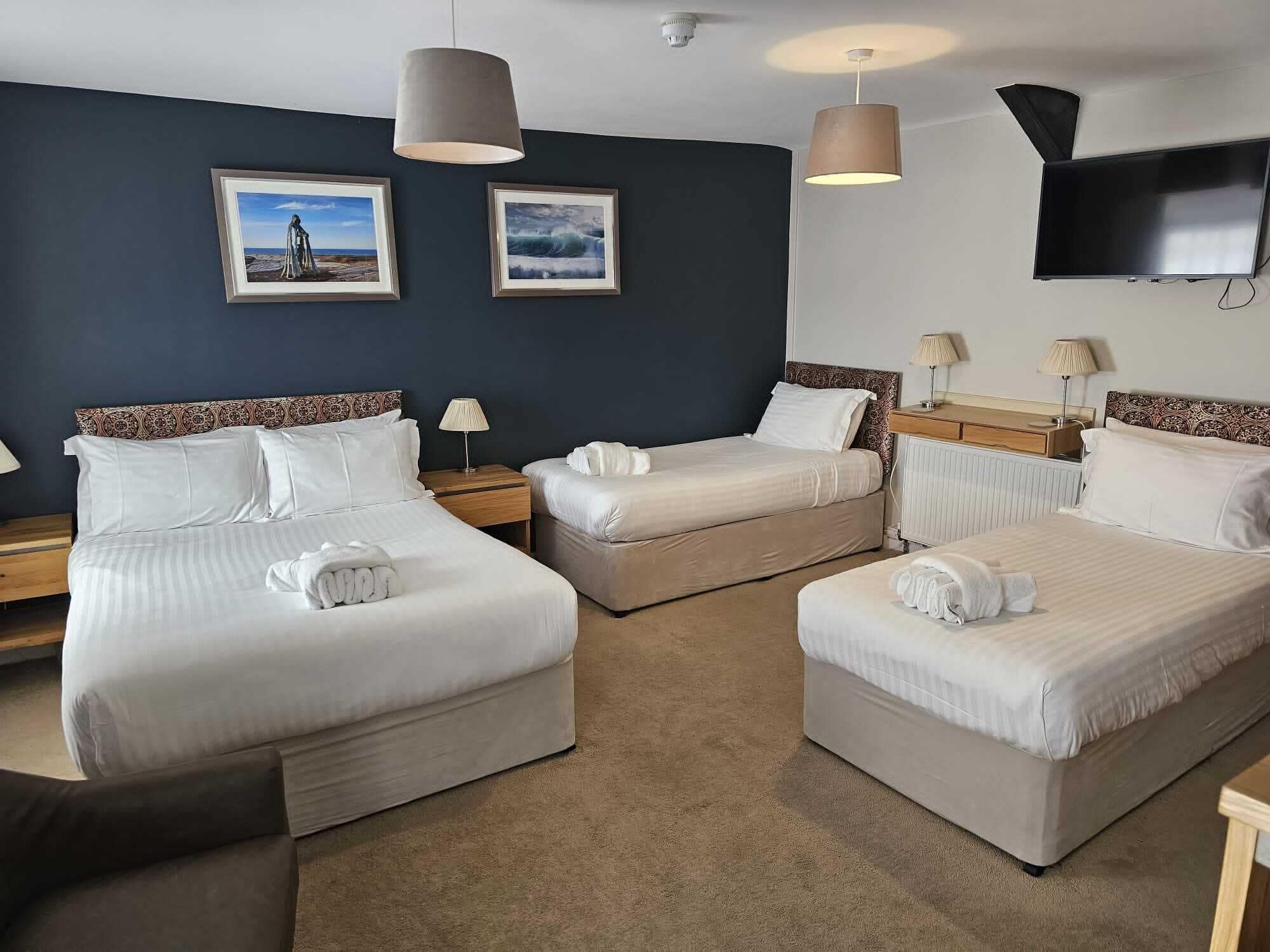 Ein Hotelzimmer mit drei Betten, einem Flachbildfernseher und zwei gerahmten Bildern an der Wand.