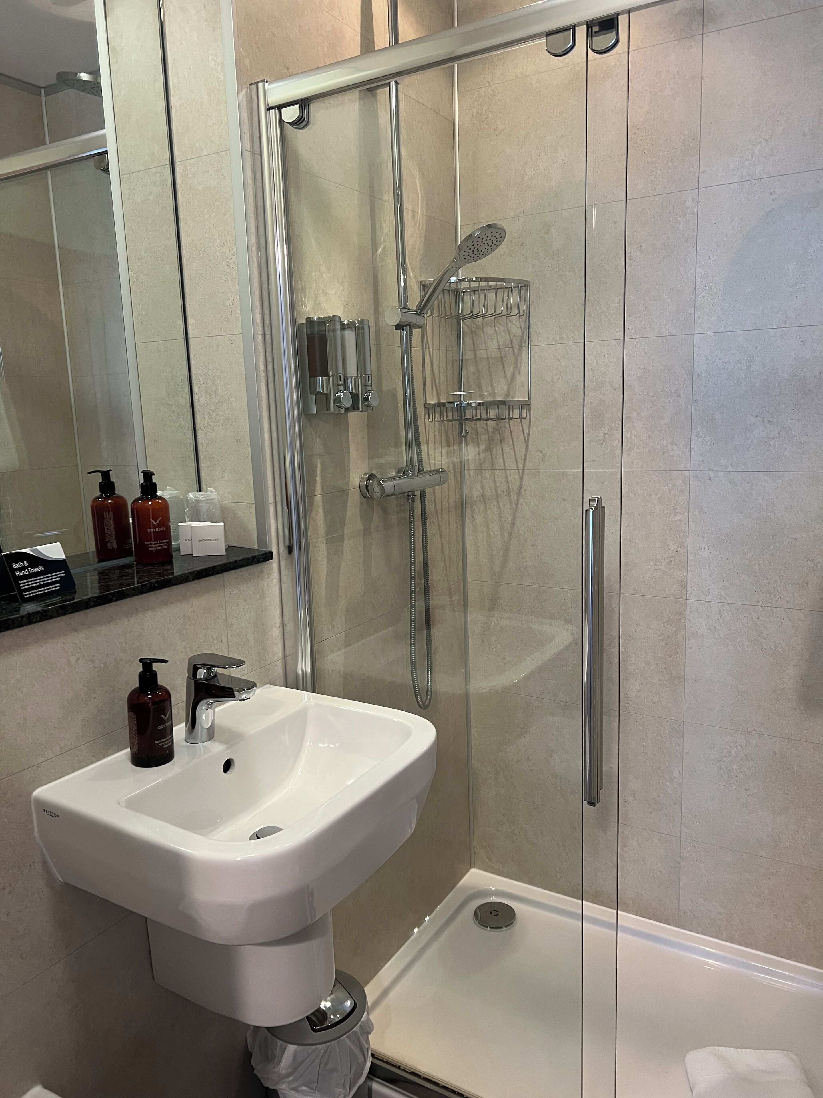 Un baño moderno con ducha envuelta en vidrio, un lavabo blanco y un cabezal de ducha de mano.