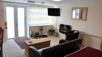 Une chambre d’hôtel comprenant un lit, un bureau, une chaise, une télévision, une fenêtre avec des stores et une porte.