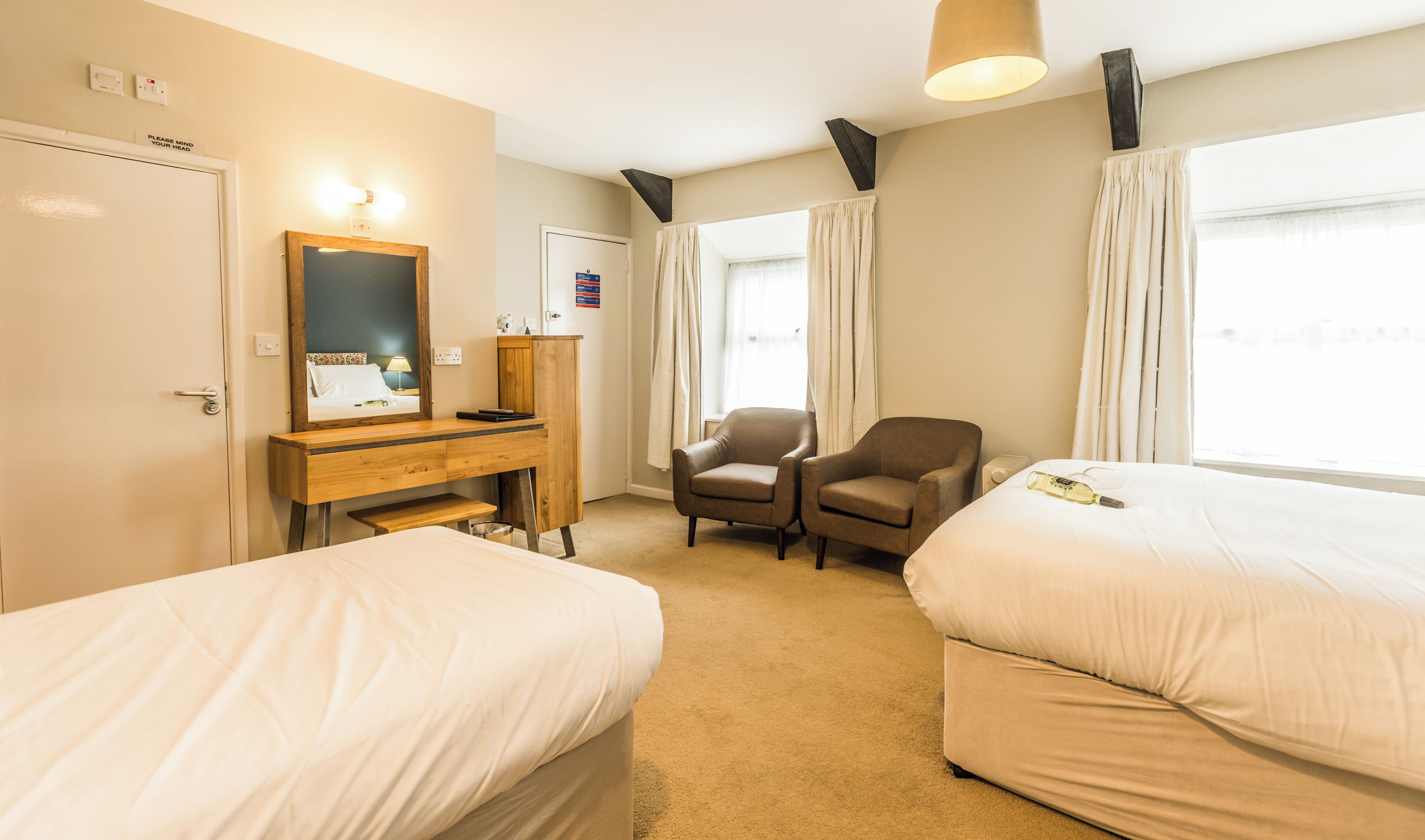 A hotel room with two beds, a desk with a mirror, a chair, and a window with curtains.