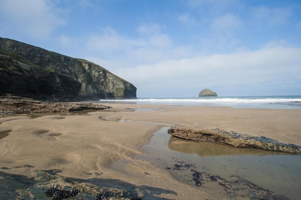 Une plage au terrain rocheux, avec une grande formation rocheuse visible au loin.