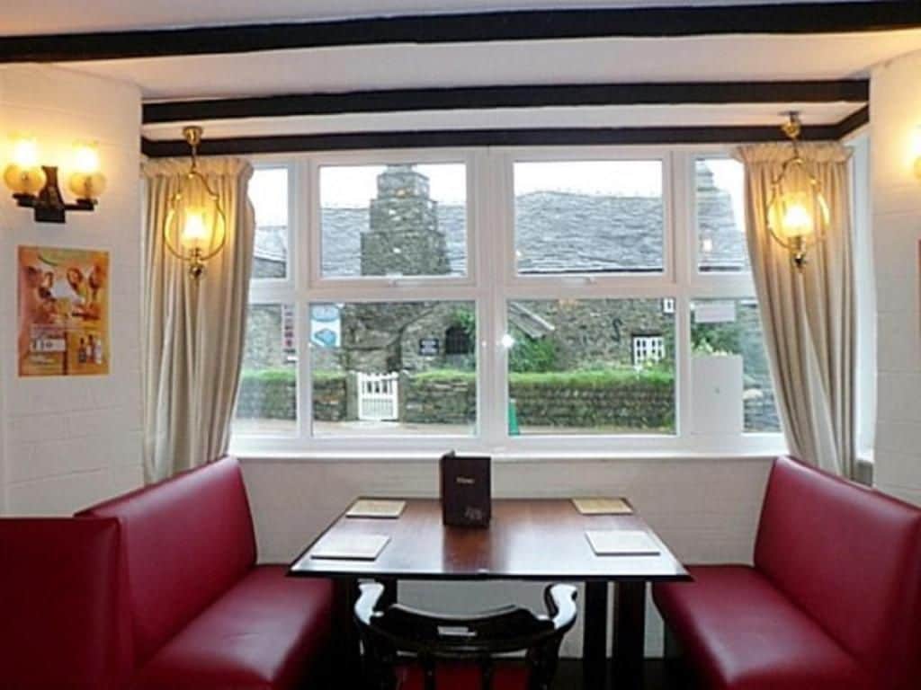 A restaurant with a table and red booth seating, large windows with curtains, and a view of a building outside.