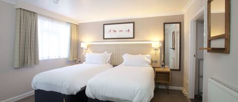 A hotel room with two beds, a bedside table, a mirror, and a framed picture on the wall.