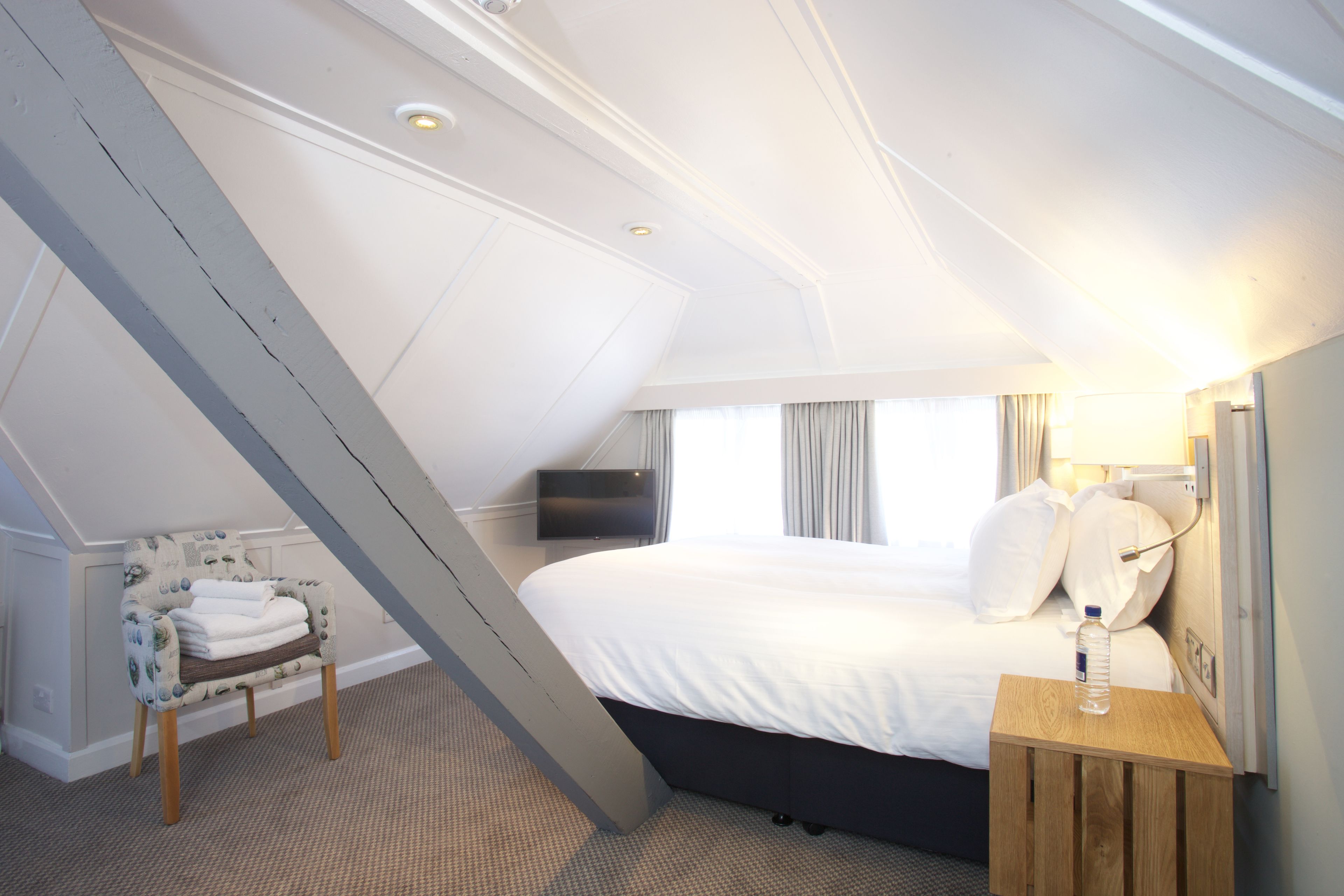 A hotel room with a bed, a chair, a bedside table, a TV, and a window with curtains.