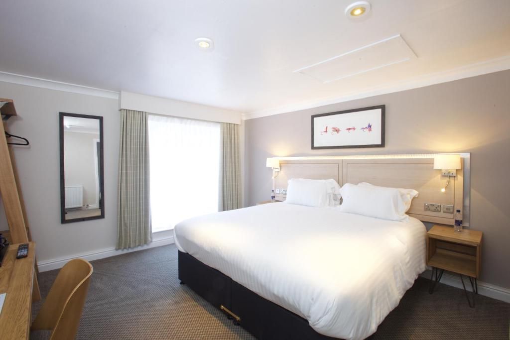 A hotel room with a large bed, bedside tables, a mirror, and a window with curtains.