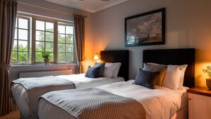 A hotel room with two beds, a large window with curtains, a painting on the wall, and a bedside lamp. - The Carpenters Arms (Tonbridge)