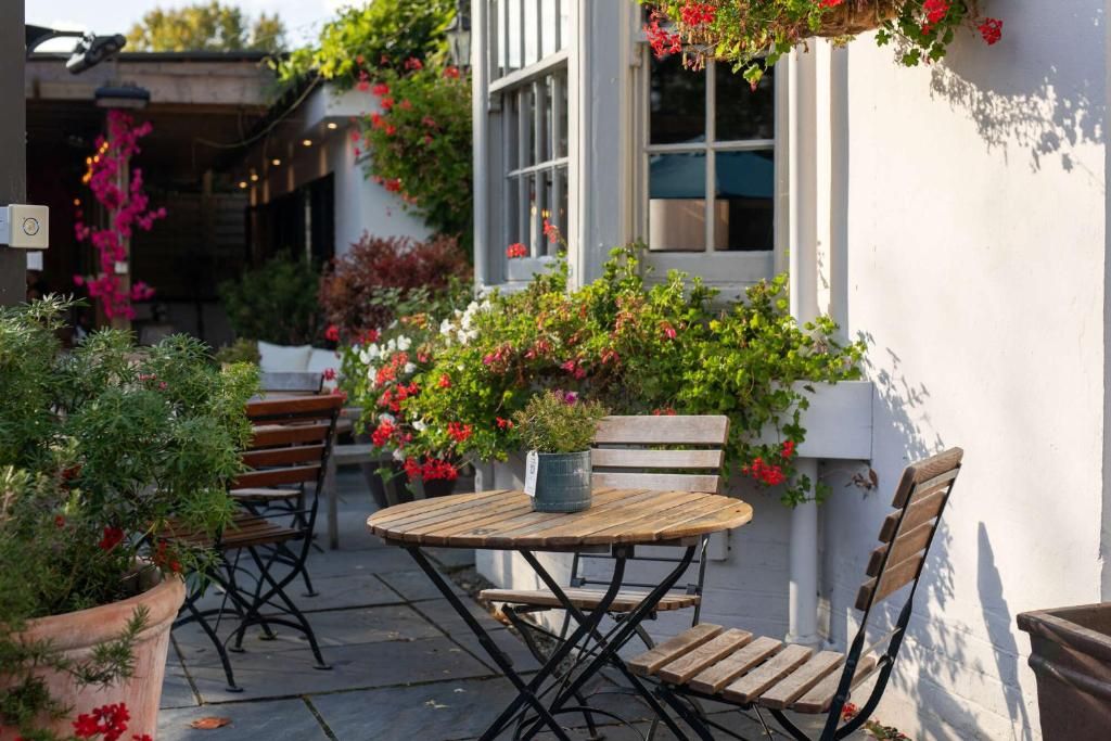Un espace extérieur aménagé avec une table ronde en bois et deux chaises en bois, entouré de plantes et de fleurs en pot.