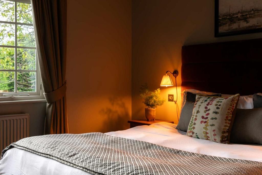 A bedroom with a bed, a bedside lamp, a window with curtains, and a wall-mounted picture.