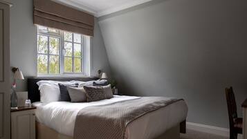 Un dormitorio con una cama, mesitas de noche, una ventana con cortinas y una silla.