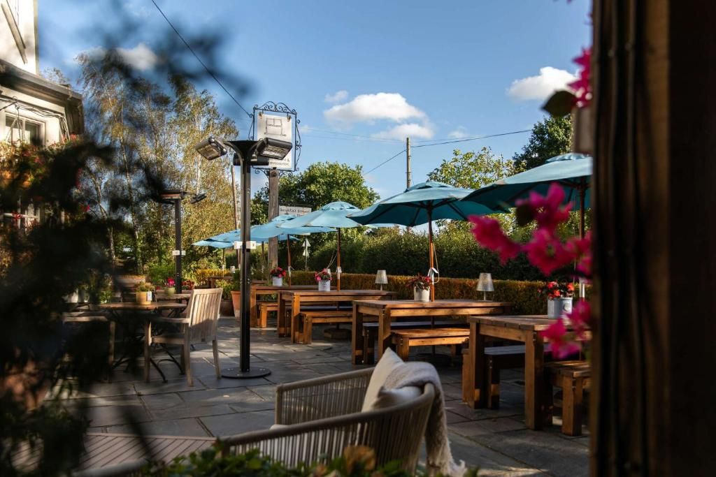 Un espace extérieur aménagé avec des tables et des parasols, entouré de verdure et surplombé par un ciel dégagé.