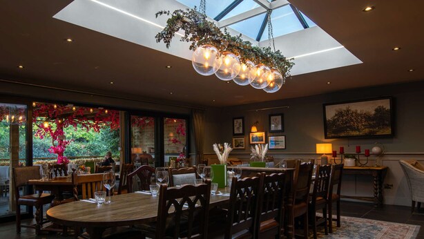A dining area with a high ceiling, a skylight, and a chandelier. There are tables and chairs arranged for dining. - The Carpenters Arms (Tonbridge)