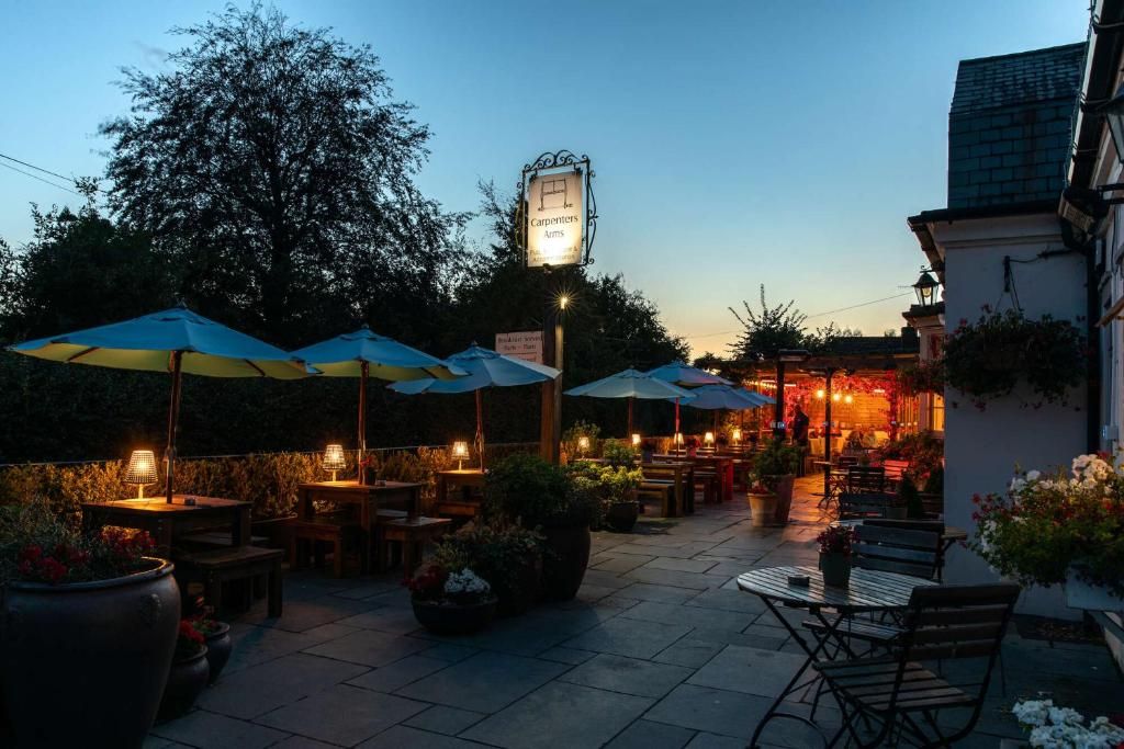 An outdoor patio area with tables and chairs, umbrellas, and a sign for 'Carpenters Arms.'