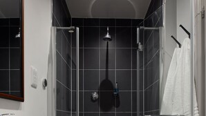 A modern bathroom with a white sink, dark tiled walls, and a glass shower enclosure. - The Carpenters Arms (Tonbridge)