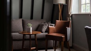 A modern living room with a sofa, a leather chair, a small round table with a plant, and a floor lamp. - The Carpenters Arms (Tonbridge)