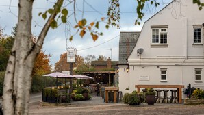 A building with a sign for carpentry tools, outdoor seating with umbrellas, and potted plants. - The Carpenters Arms (Tonbridge)